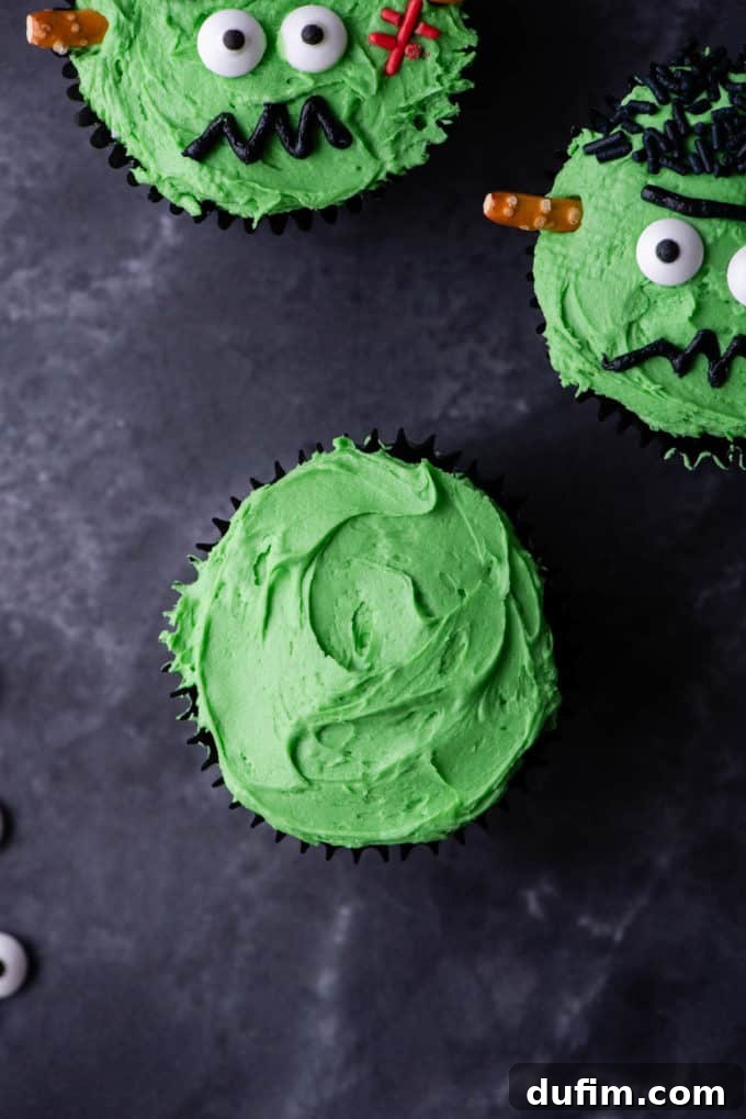 A cupcake freshly frosted with green, next to two fully decorated Frankenstein cupcakes, illustrating the first step of frosting.