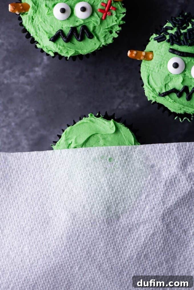 A Frankenstein cupcake with green frosting and black jimmie sprinkles for hair, demonstrating the second step of decoration.