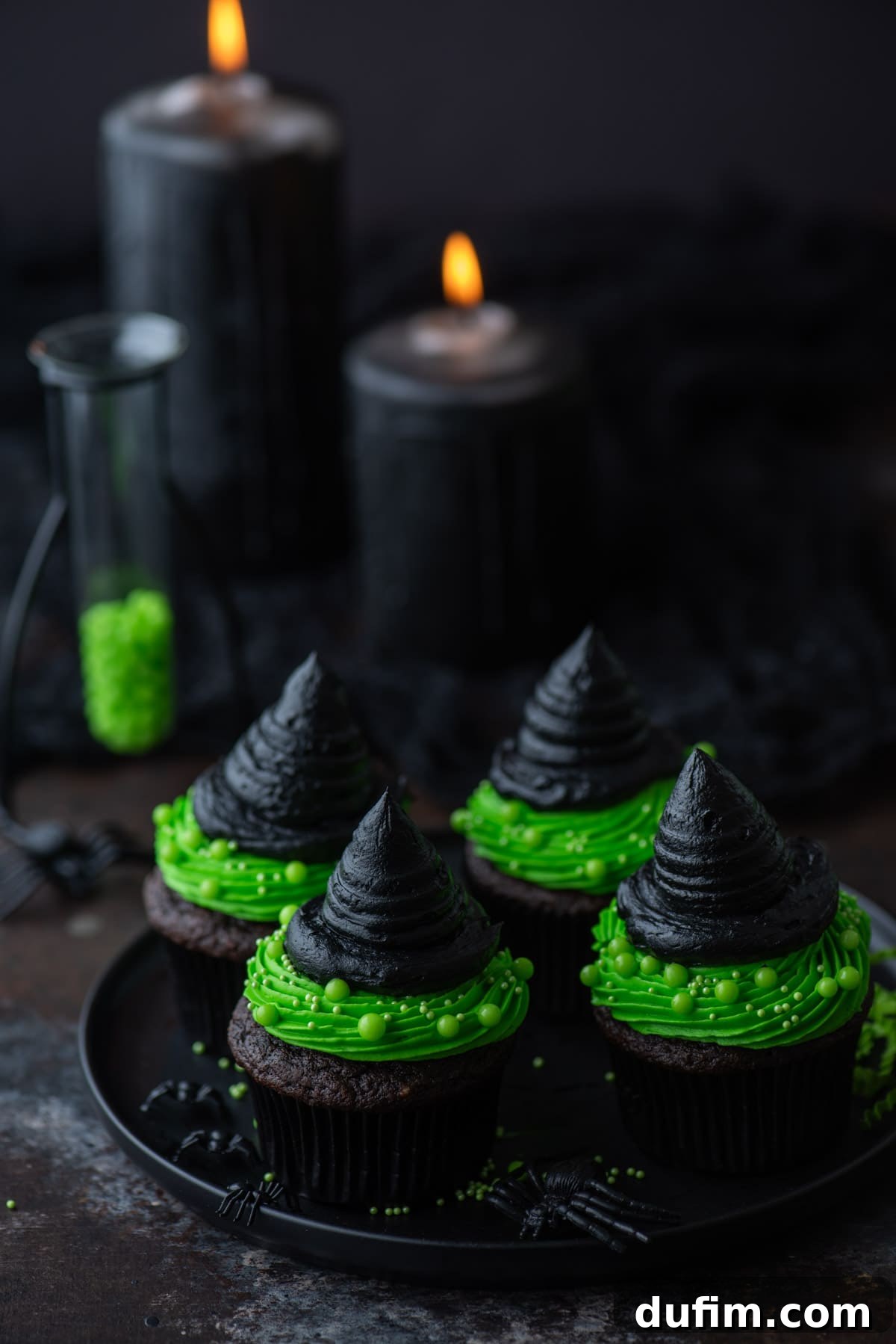Witch hat cupcakes on a black plate with black candles in the background, showcasing vibrant green and black frosting on chocolate cupcakes.