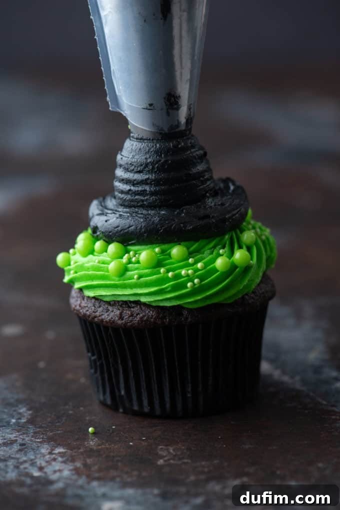 A chocolate cupcake with bright green frosting, a black frosting brim, and the beginning of a pointed black frosting hat being piped in an upward motion.