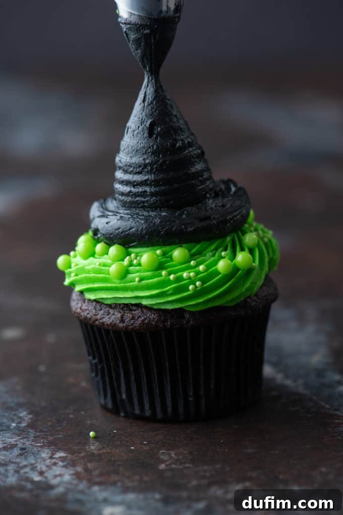 A finished witch hat cupcake, showing the vibrant green base, the detailed black brim, and the sharply pointed black hat, ready to be served.