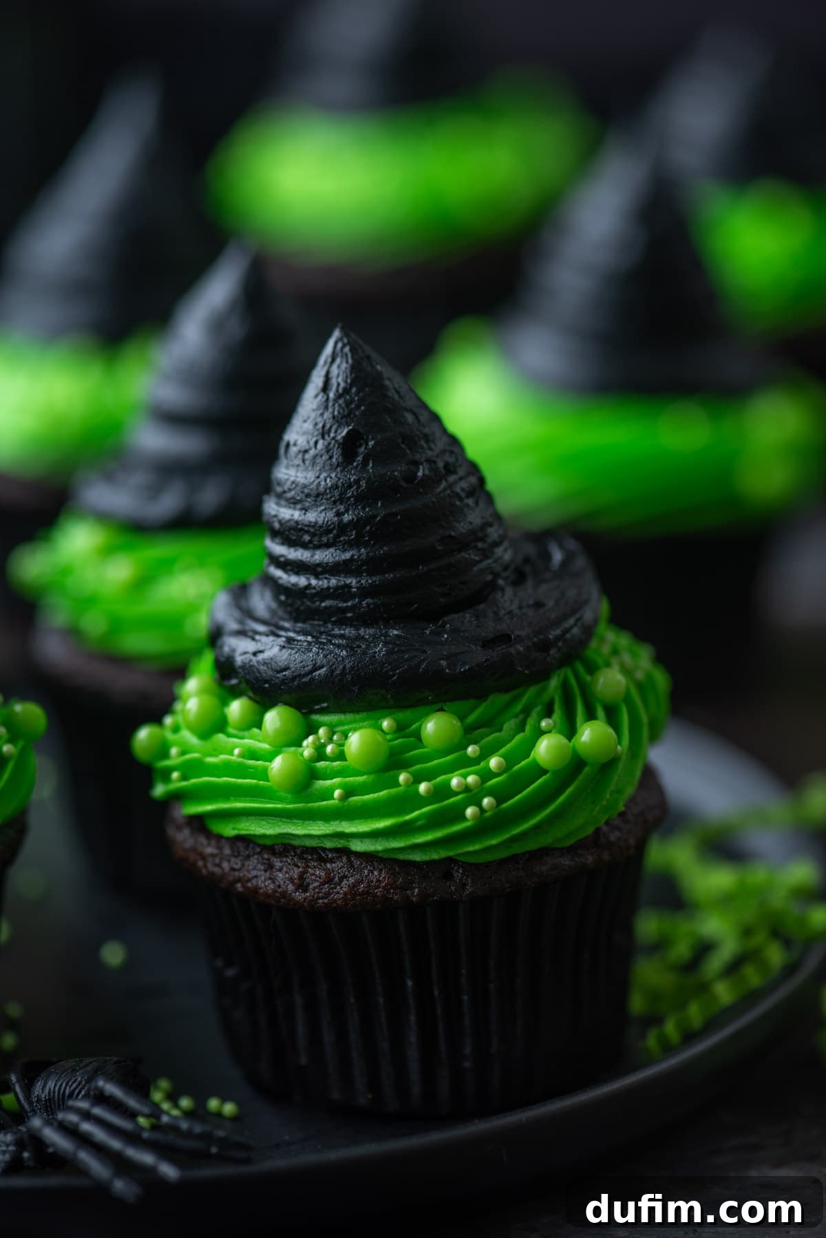 Green and black witch hat cupcakes arranged on a dark plate, ready for a Halloween celebration.