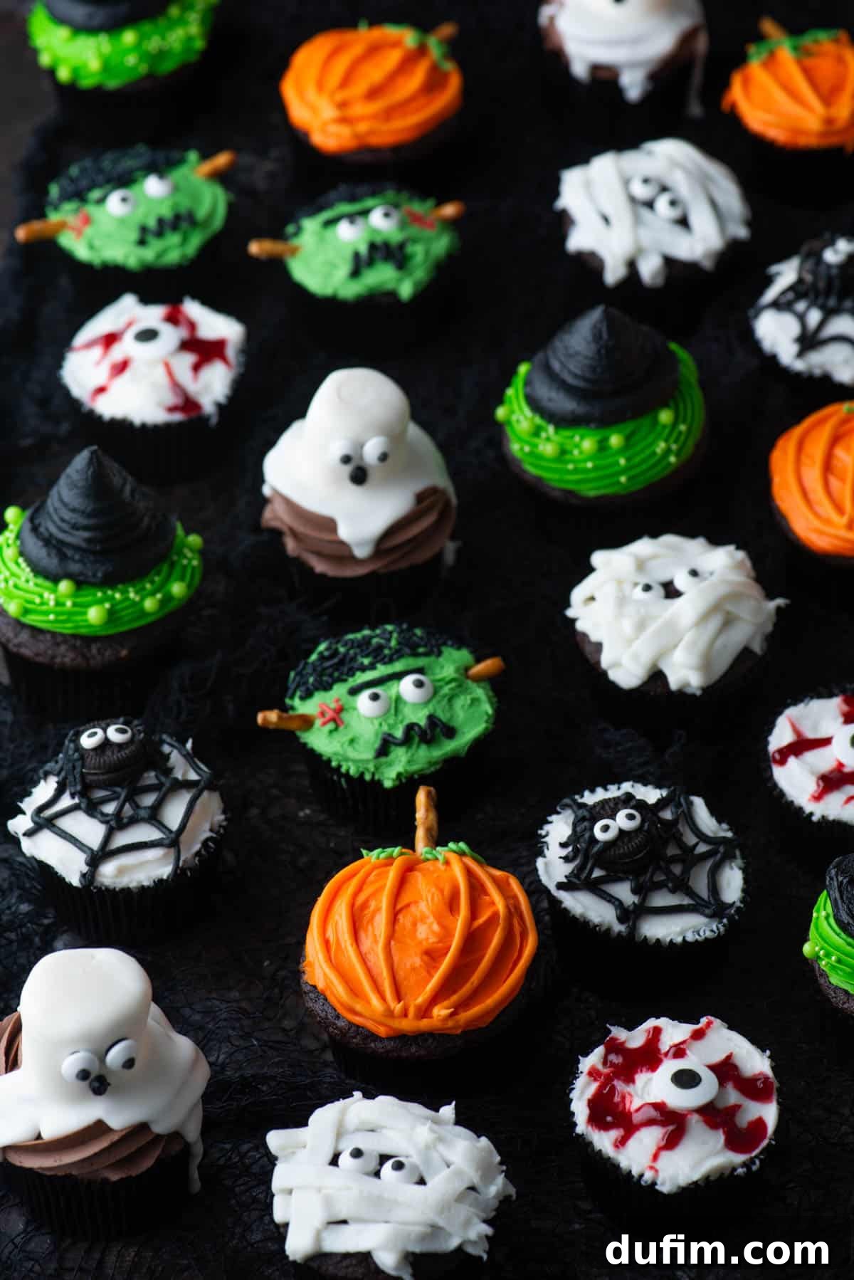 Ghoulishly Good Cupcakes 2 An assortment of Halloween cupcakes featuring mummy, ghost, pumpkin, Frankenstein, spider, eyeball, and witch hat designs, perfectly arranged for a festive display.