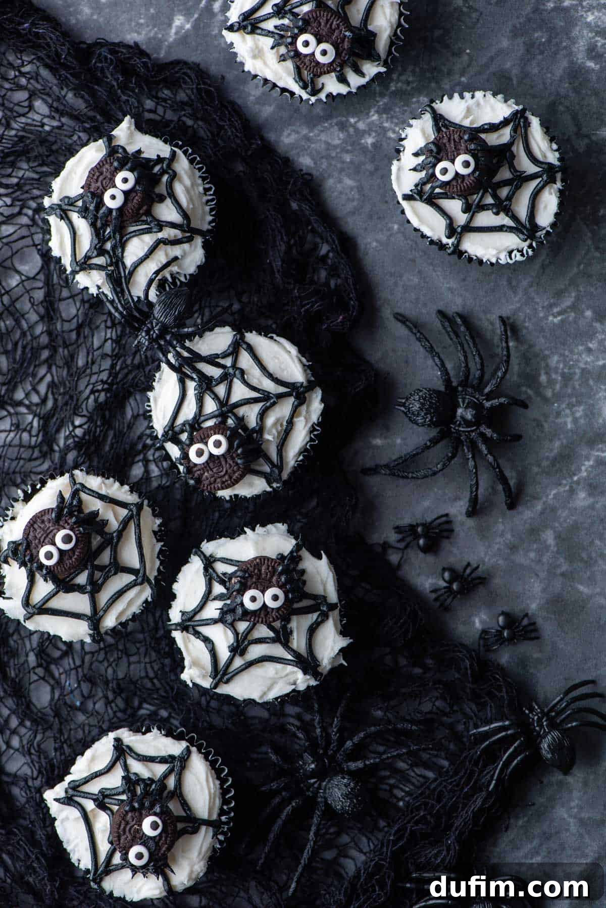 Ghoulishly Good Cupcakes 15 Spider web cupcakes gracefully positioned on a black netting, surrounded by scattered black plastic spiders, enhancing the spooky Halloween atmosphere.
