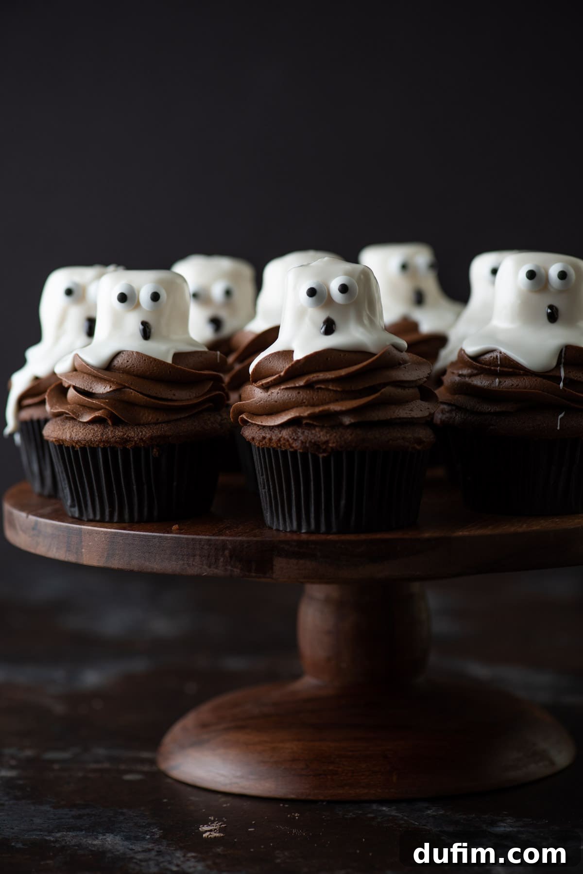 Ghoulishly Good Cupcakes 17 Whimsical ghost cupcakes displayed on an elegant wooden cake stand, ready to be enjoyed at a festive gathering.