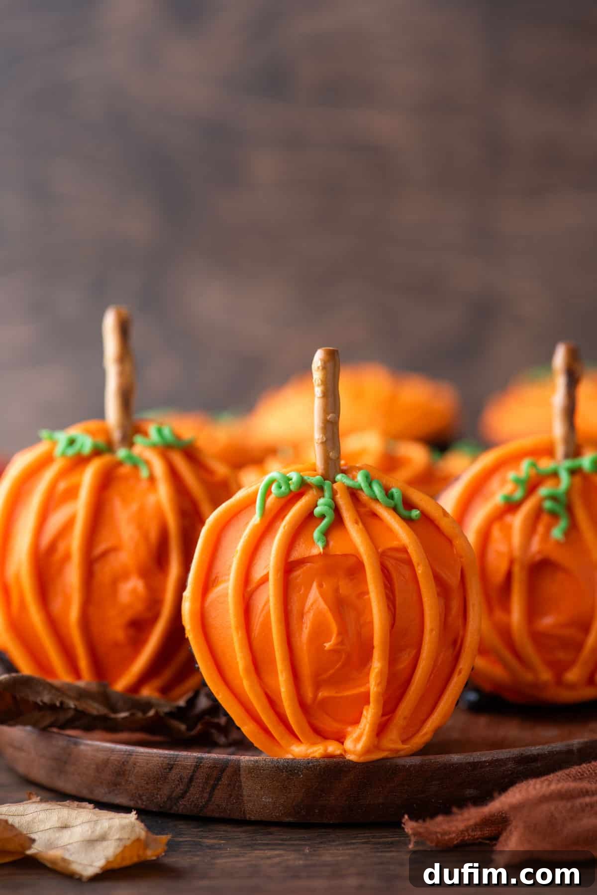 Ghoulishly Good Cupcakes 7 Charming pumpkin patch cupcakes displayed on a rustic wooden plate, standing upright to showcase their pretzel stick stems, evoking a cozy autumnal feel.