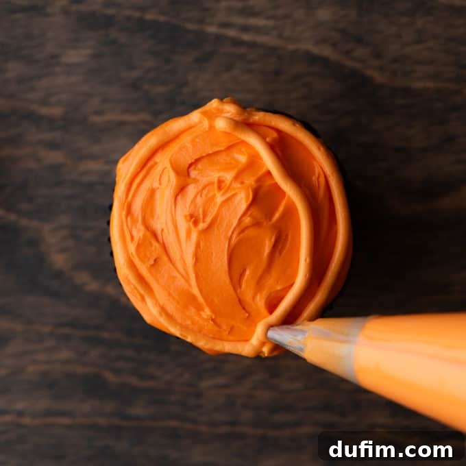 A cupcake with orange frosting now features multiple curved orange lines, shaping it into a recognizable pumpkin on a wooden backdrop.