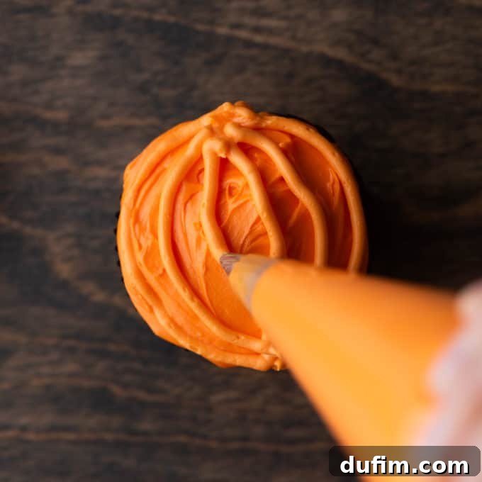 A close-up of a fully piped orange pumpkin cupcake, showing all the curved lines that define its shape, sitting on a wooden surface.
