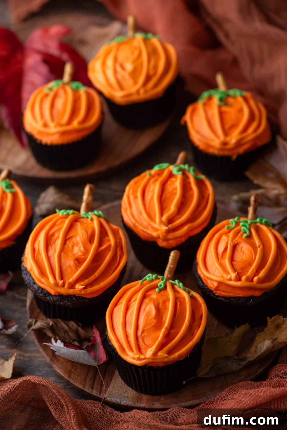 A festive arrangement of pumpkin patch cupcakes on wooden plates, surrounded by autumn leaves, evoking a warm fall atmosphere.