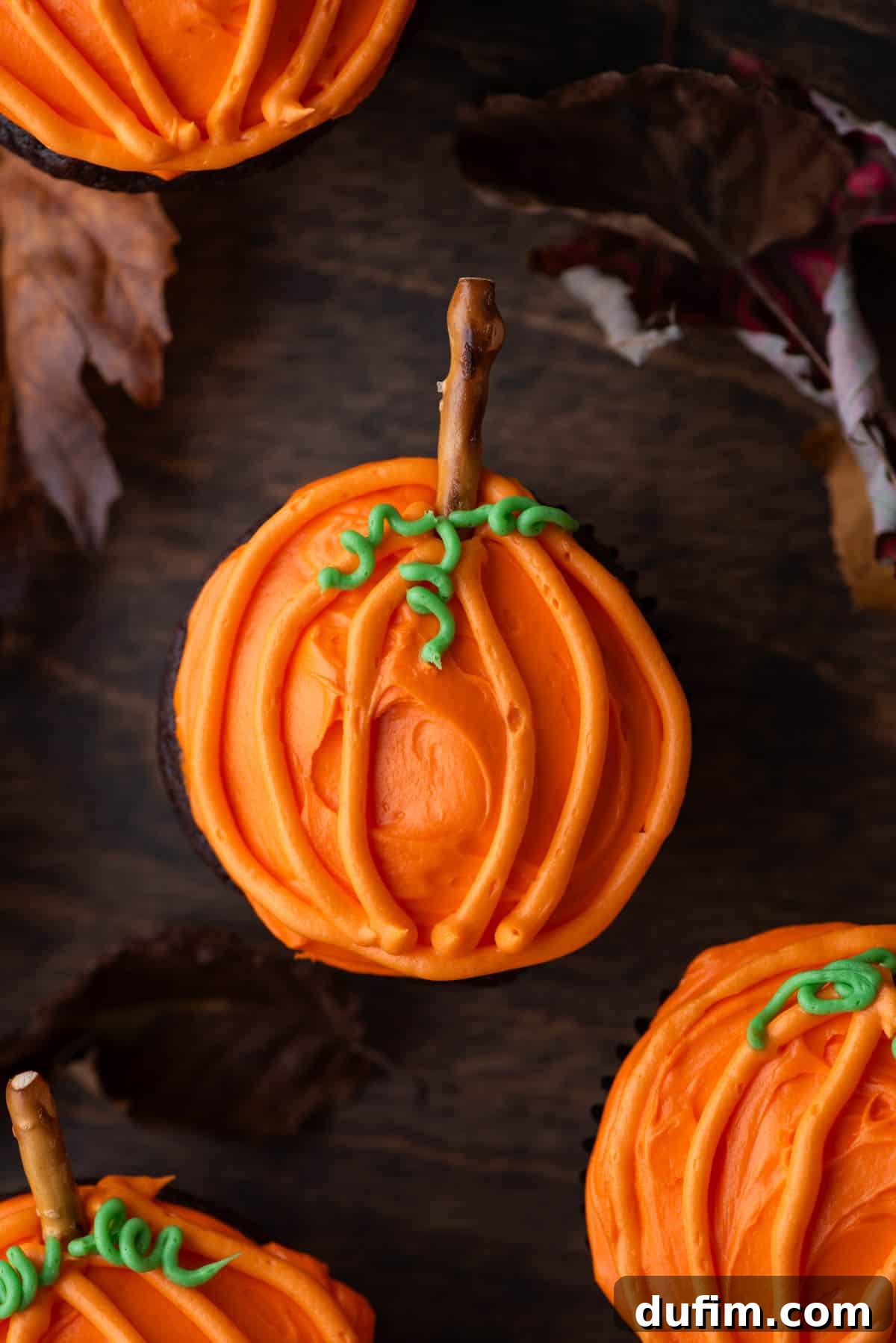 A close-up shot of pumpkin patch cupcakes arranged on a wooden surface, surrounded by vibrant fall leaves, highlighting their festive appeal.