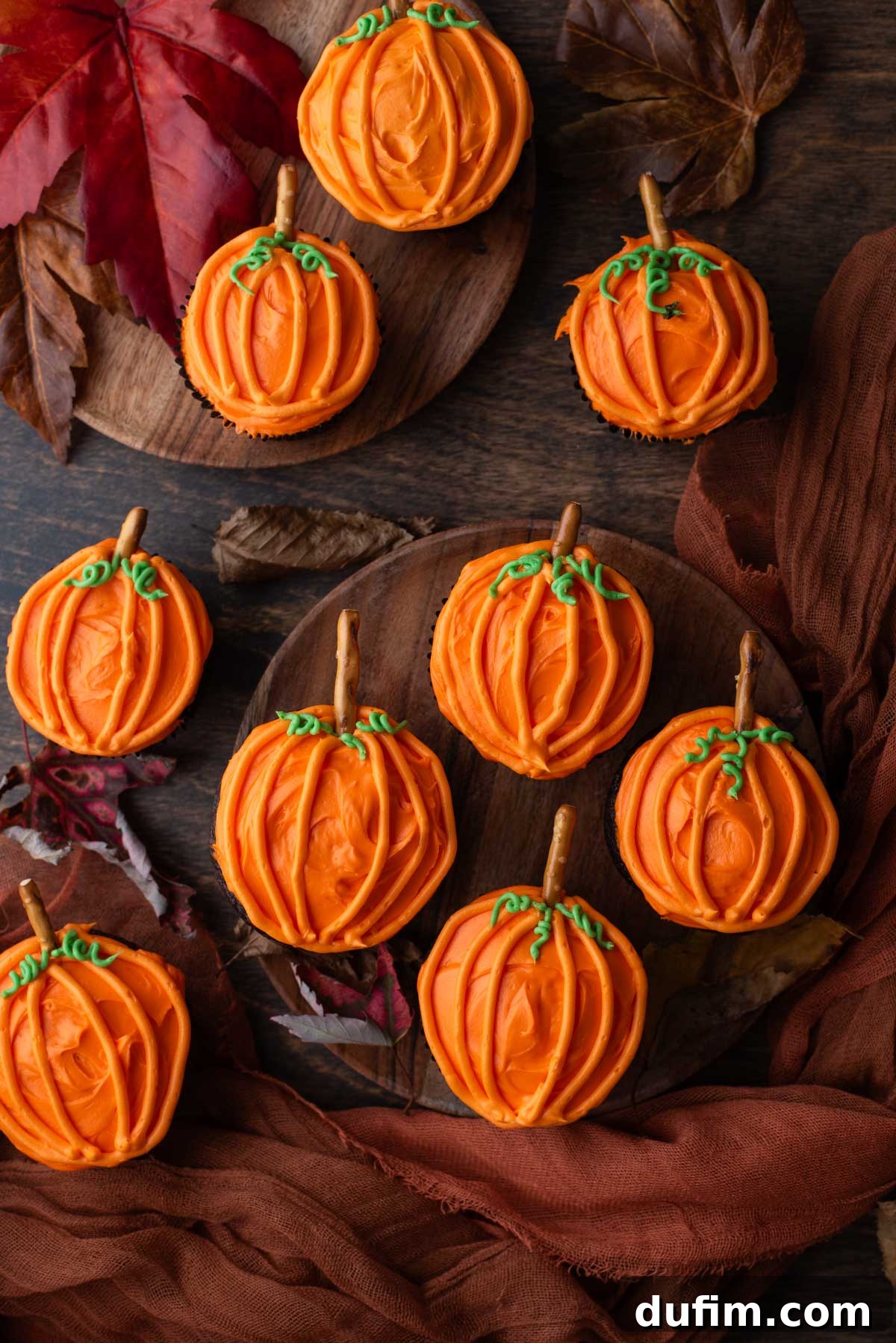 An inviting display of pumpkin patch cupcakes arranged artfully on wooden plates, surrounded by colorful autumn foliage.