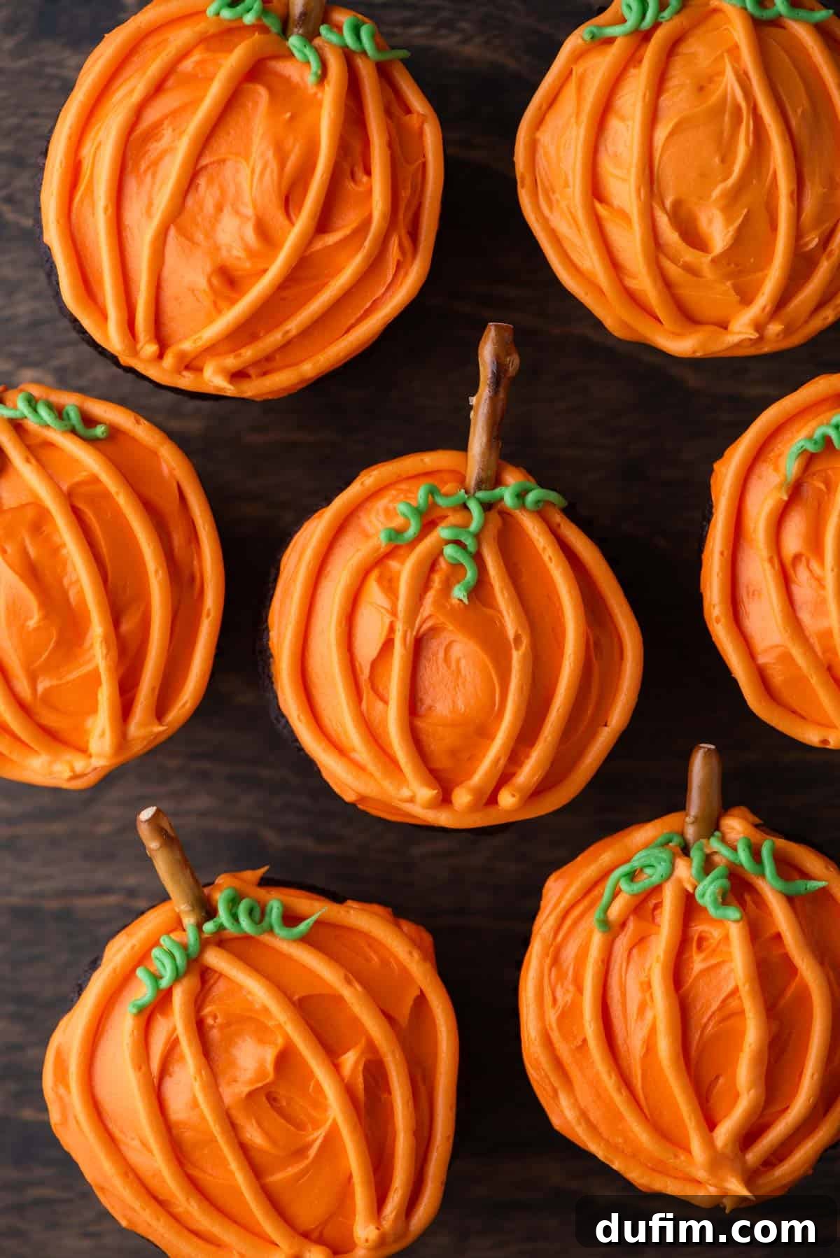 A delicious pumpkin patch cupcake resting on a rustic wooden surface, showcasing its vibrant orange frosting and pretzel stem.