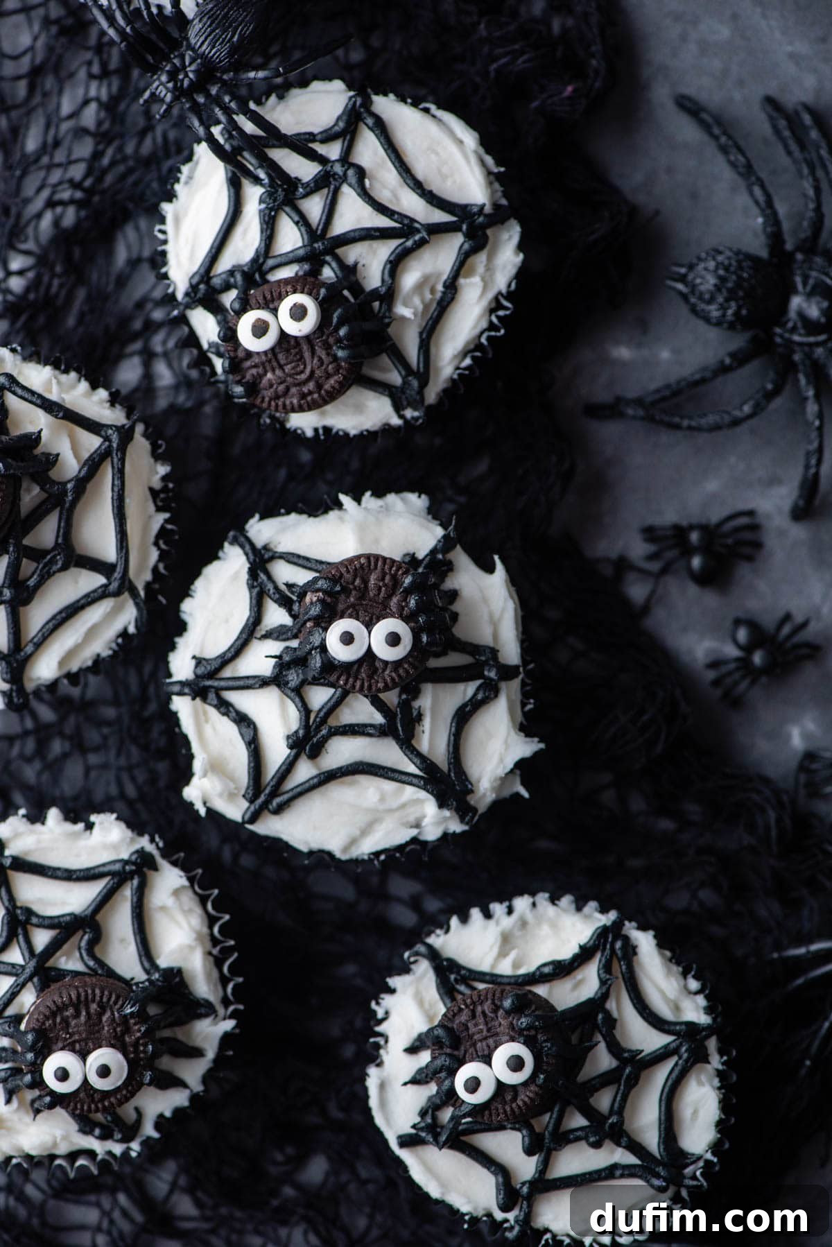 Delicious spider web cupcakes beautifully arranged on a black netting, surrounded by small plastic black spiders for a spooky Halloween display.