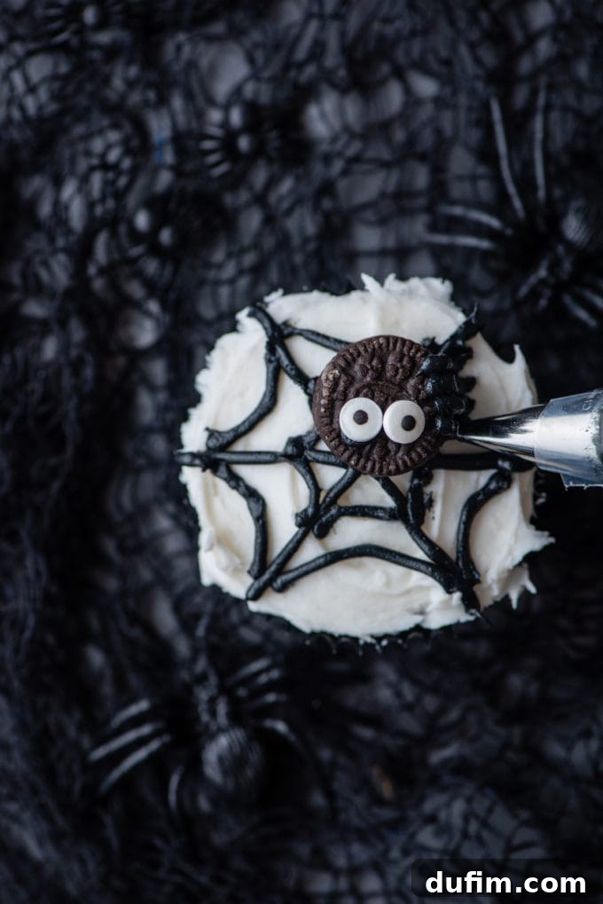 The final step of piping eight delicate legs onto the mini Oreo to complete the edible spider on a spider web cupcake.