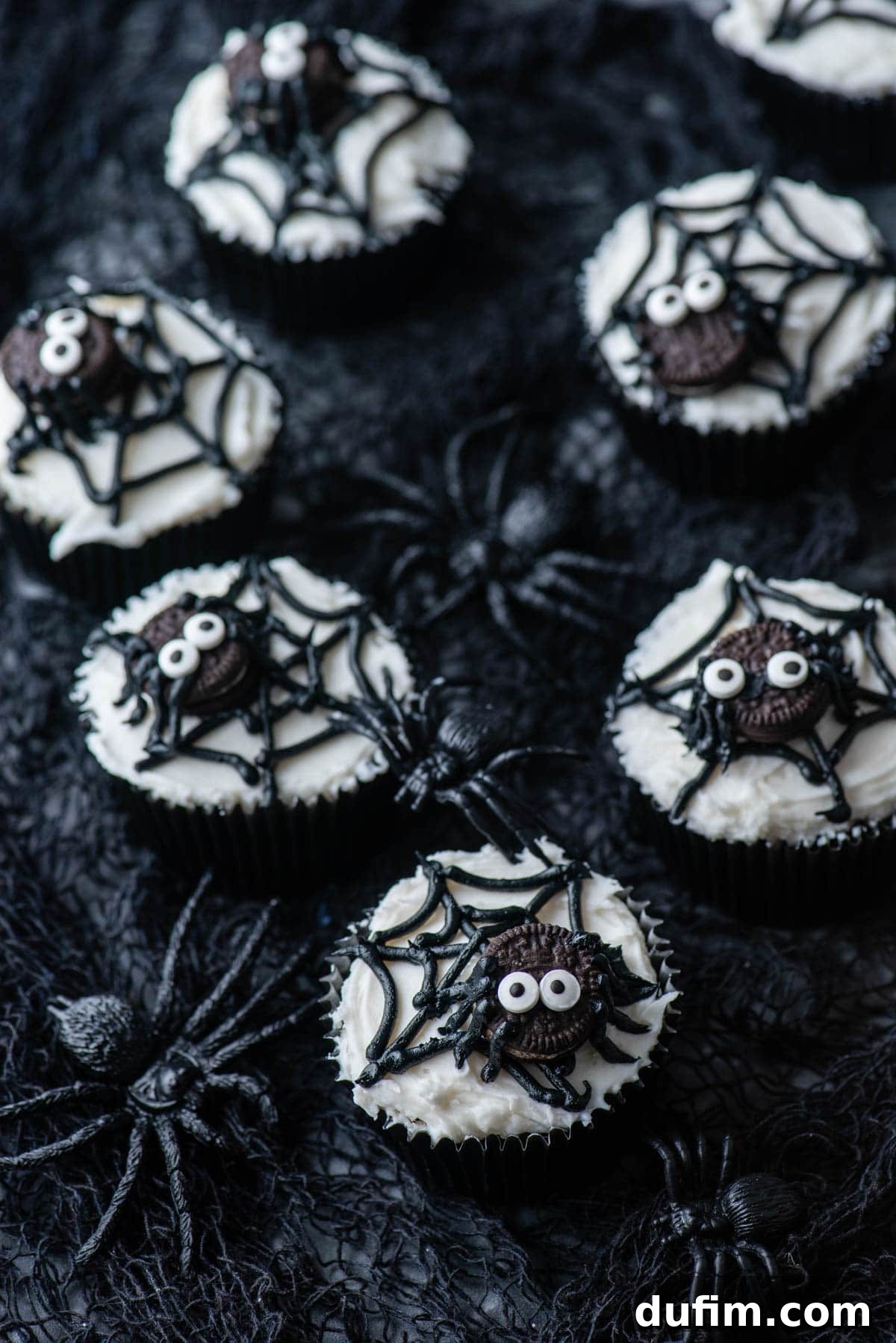 A collection of spider web cupcakes arranged artfully on a black netting, with plastic black spiders scattered around them for a spooky effect.