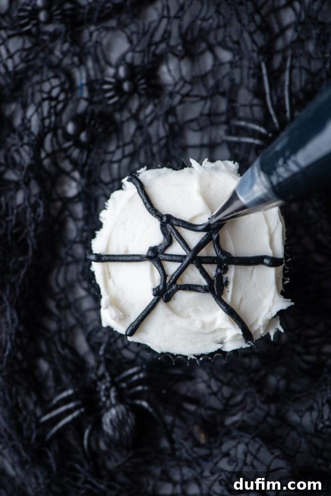 Adding two diagonal black lines to form an 'X' over the first horizontal line, further developing the spider web pattern on the cupcake.