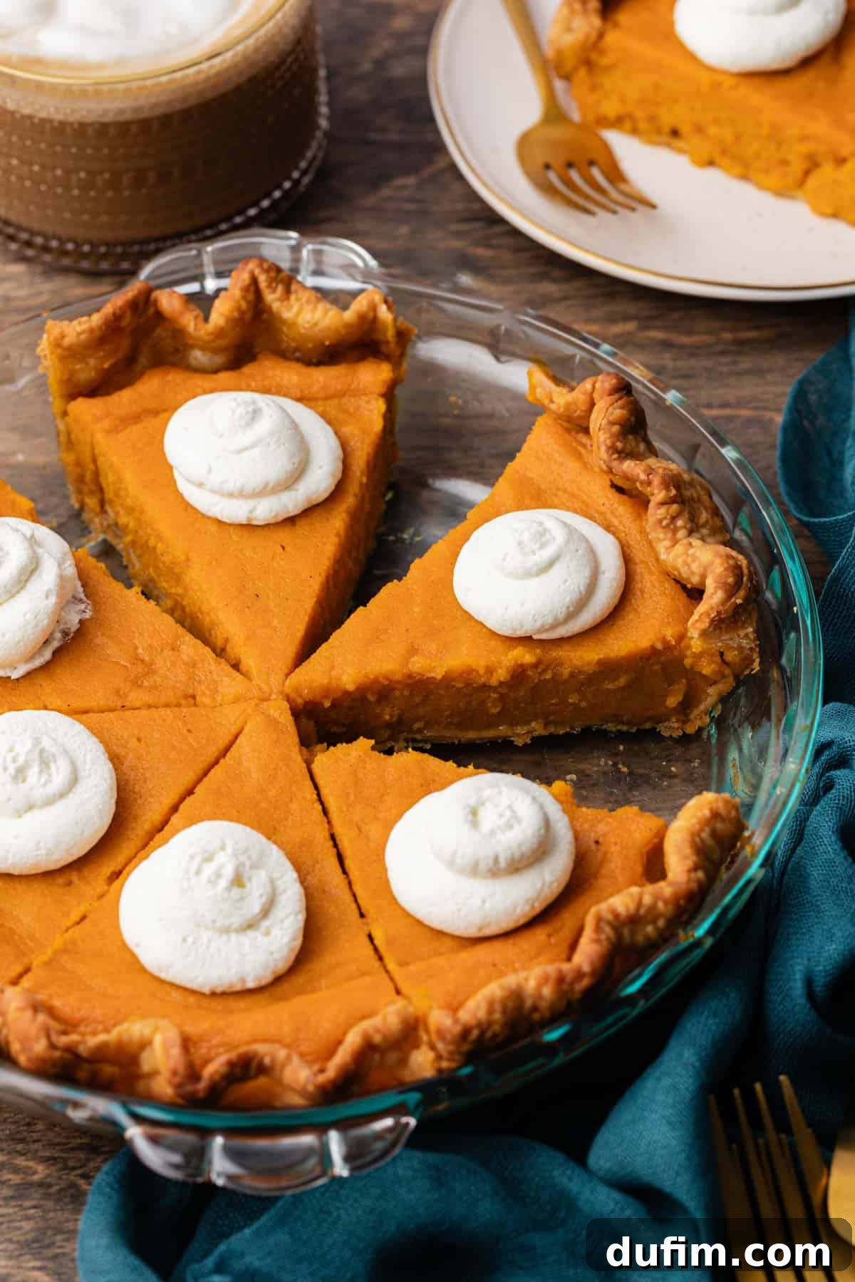 Grandma's Secret Sweet Potato Pie Recipe 2 sweet potato pie slices in a glass pie dish, a dark teal towel, fork and white plate with a slice of pie on it in the background