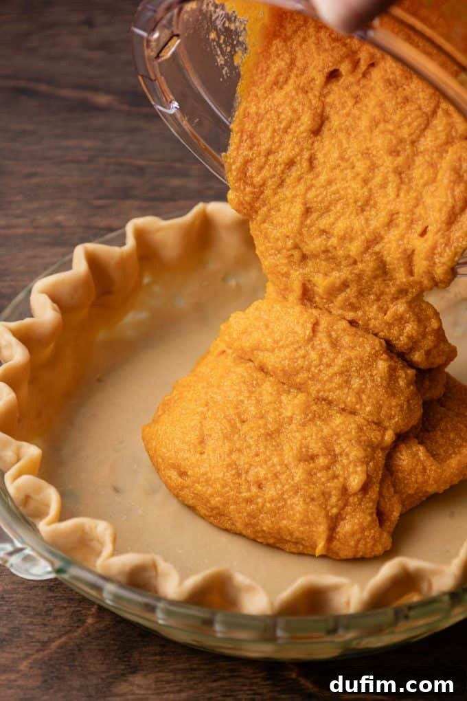 Grandma's Secret Sweet Potato Pie Recipe 11 sweet potato pie filling being poured into a pie crust in a glass pie dish sitting on a wood surface