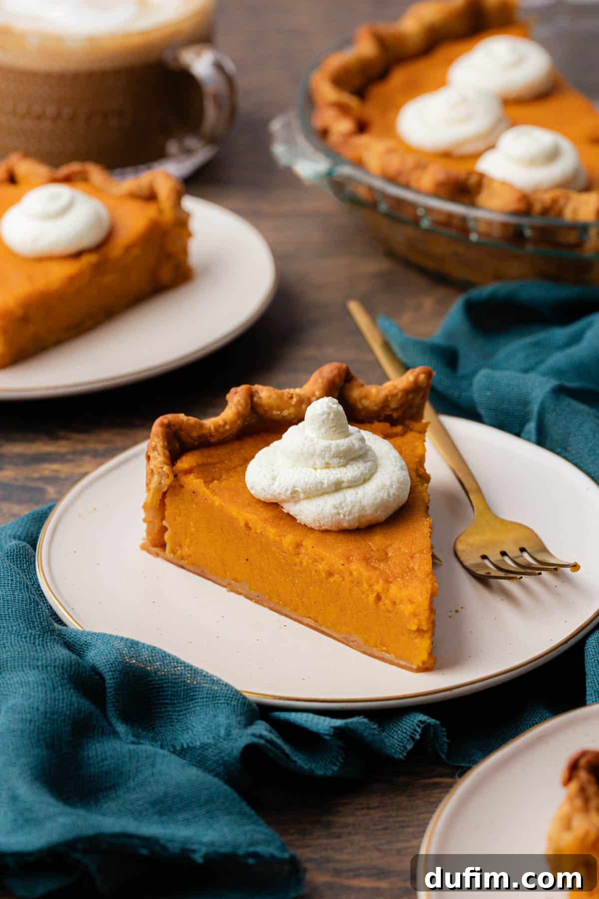 Grandma's Secret Sweet Potato Pie Recipe 13 slices of sweet potato pie on white plates topped with dollops of whipped cream, with a fork sitting beside the pie on the front plate and a dark teal towel underneath the plate