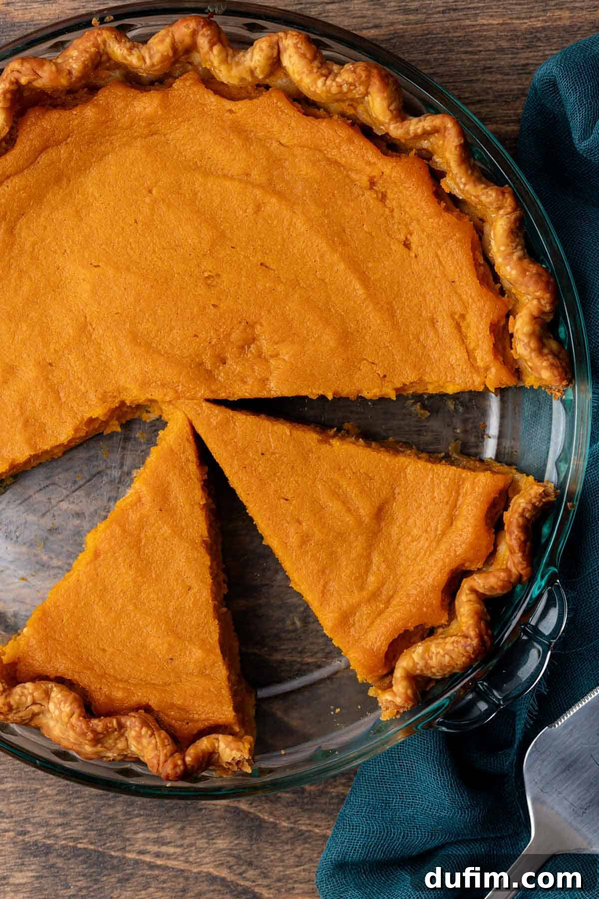 Grandma's Secret Sweet Potato Pie Recipe 15 sweet potato pie in a glass pie dish with half of it unsliced and the other half with slices missing sitting on a wood surface