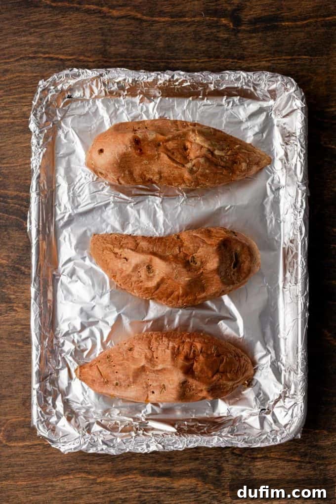 Grandma's Secret Sweet Potato Pie Recipe 7 three roasted sweet potatoes on a sheet pan covered in aluminum foil sitting on a wood surface
