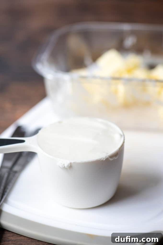 Chilled vegetable shortening in a white measuring cup on a cutting board, accompanied by two butter knives and a dish of butter cubes, showcasing the prepared fats.