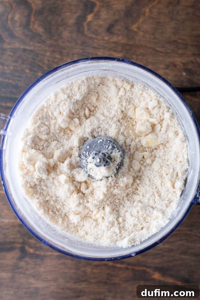 Gluten-free pie crust dry ingredients mixed in a food processor bowl, ready for the addition of cold fats, on a wooden surface.