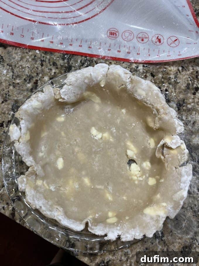 An unfinished gluten-free pie crust in a glass pie dish on a granite countertop, next to a pie mat, illustrating an early attempt.