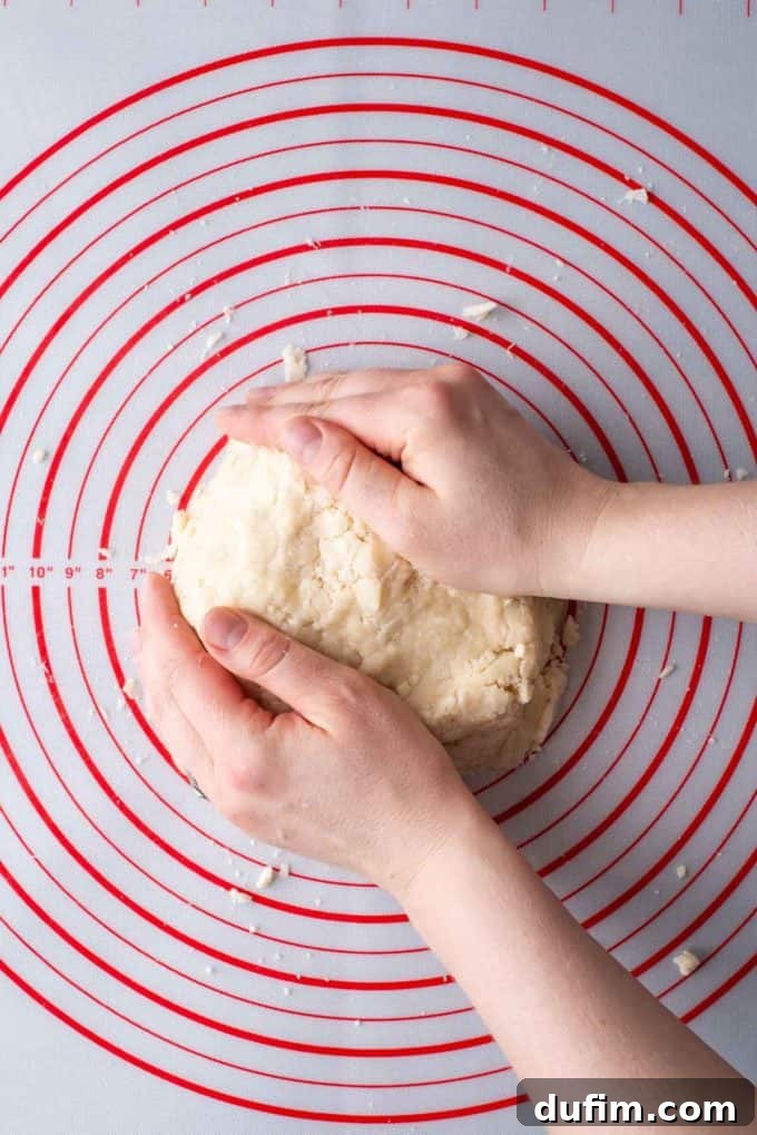 Two hands skillfully shaping a large disc of gluten-free pie crust dough on a red and white pie mat, preparing it for chilling.