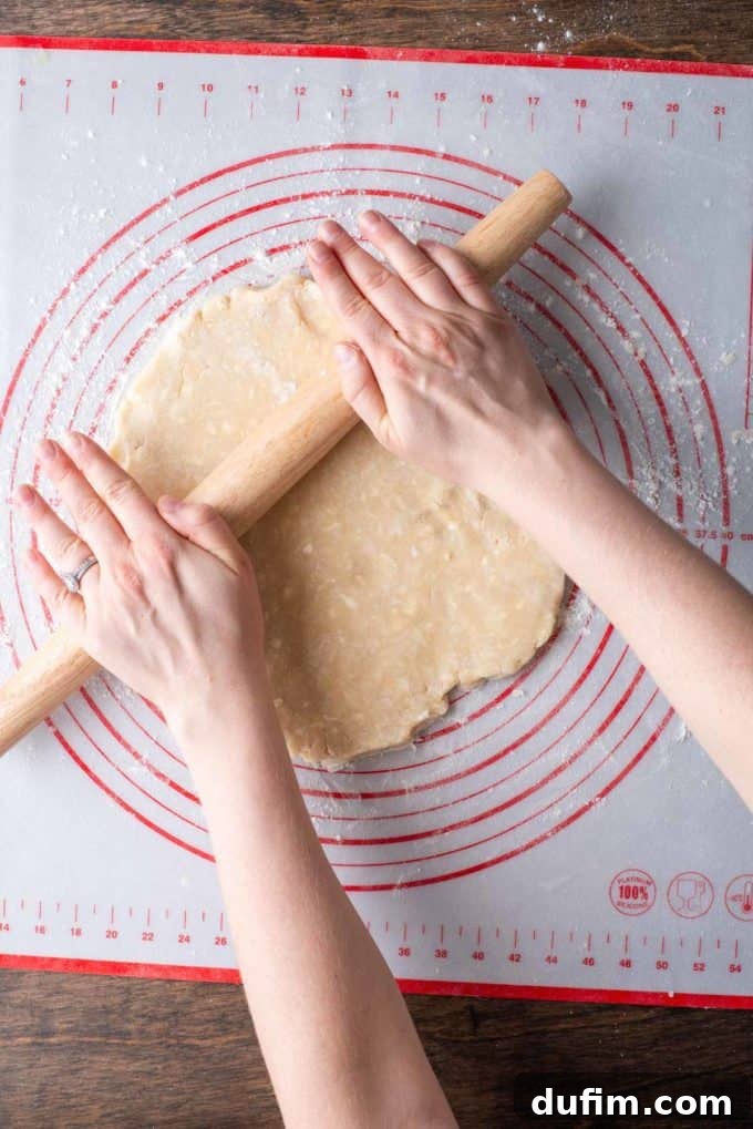 A disc of gluten-free pie crust dough being rolled out with a wooden rolling pin on a floured red and white pie mat, showcasing continued expansion.