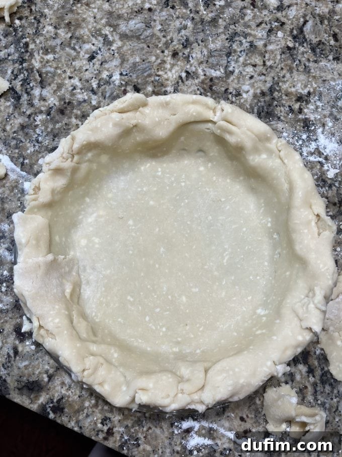 Another attempt at gluten-free pie crust in a pie pan on a granite countertop, with flour sprinkled around, showing further challenges.