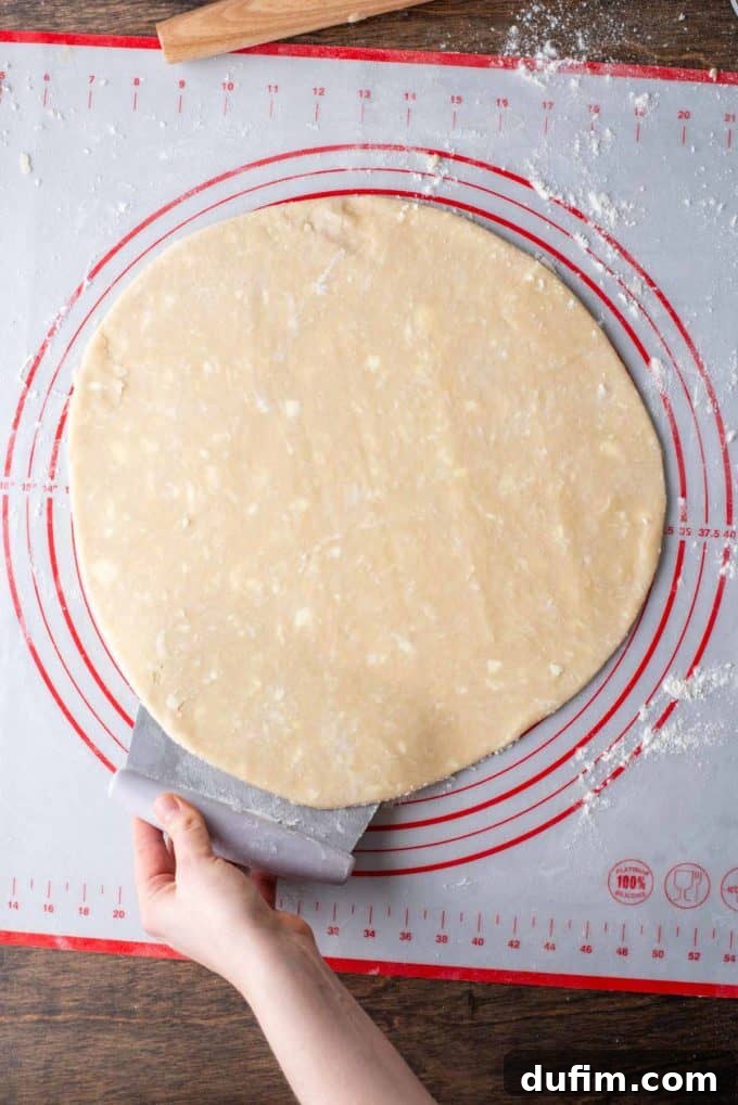 Gluten-free pie crust dough being slightly lifted from one side with a pastry cutter off the red and white pie mat it rests on.