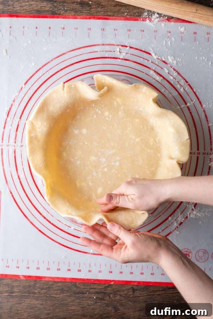 Gluten-free pie crust being carefully formed by hand into a glass pie dish, resting on a red and white pie mat, ensuring a snug fit.