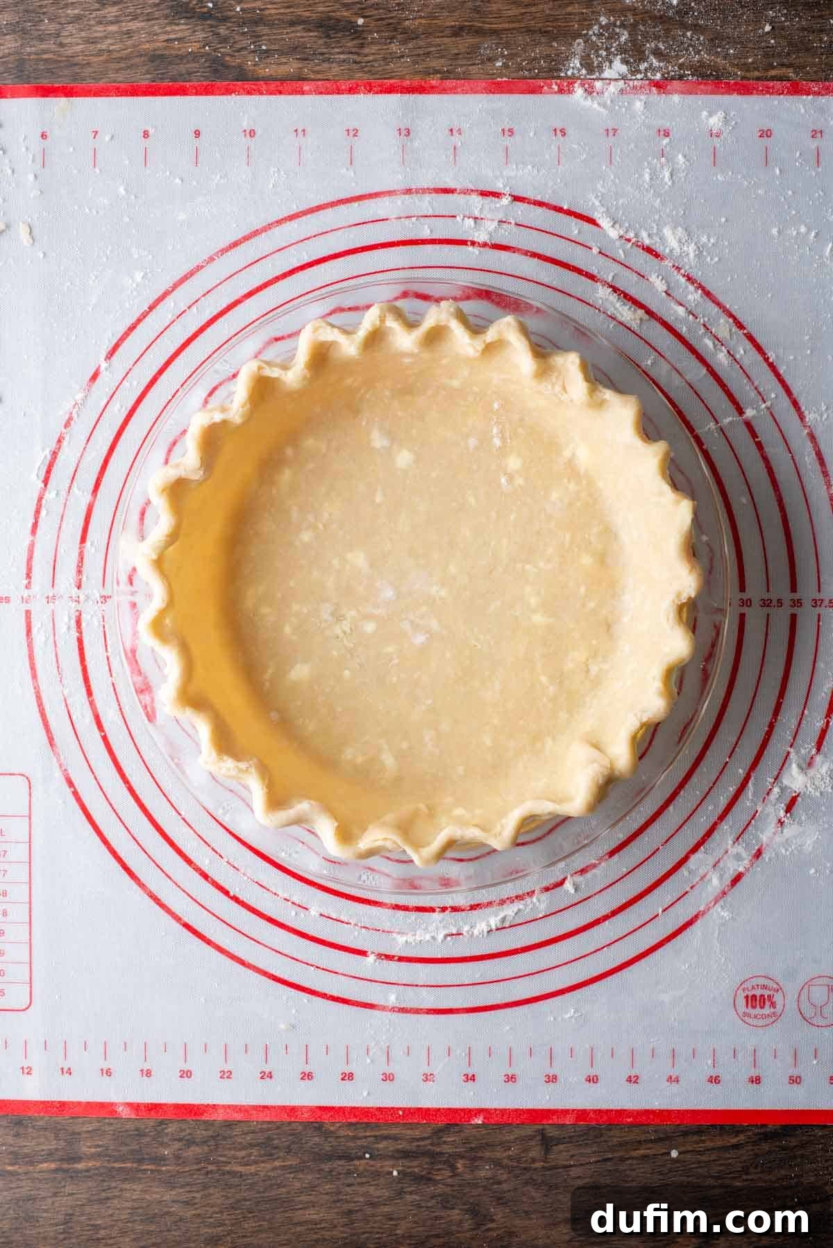 A perfectly fluted gluten-free pie crust in a pie pan, resting on a red and white pie mat with a dusting of flour, showcasing the final ready-to-bake dough.