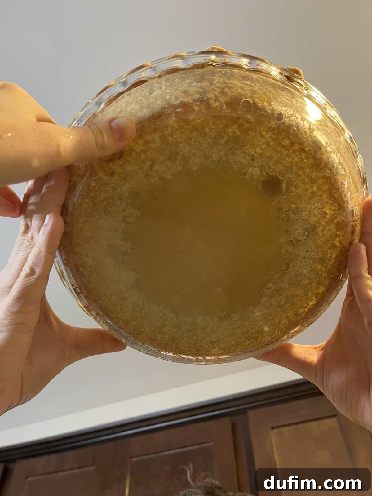 Three hands holding up a glass pie dish with a baked gluten-free pie crust, showing the underside, which was undercooked due to incorrect oven rack placement.