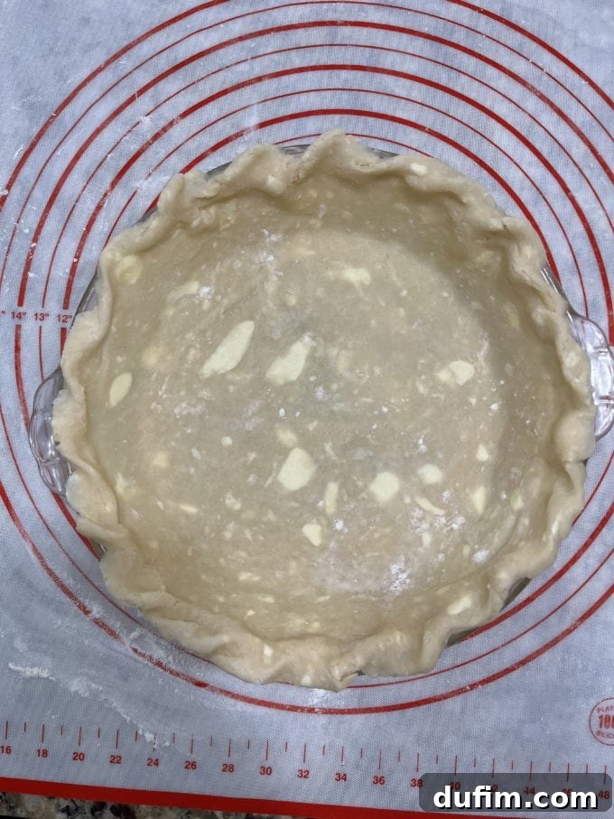 An uncooked gluten-free pie crust neatly placed in a pie dish, resting on a pie mat, demonstrating significant improvement in technique.