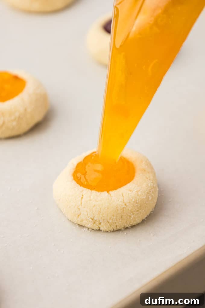 THUMBPRINT COOKIES: A TIMELESS DELIGHT 13 Thumbprint cookies on a baking sheet lined with parchment paper are being carefully filled with sweet apricot jam, showcasing the vibrant yellow hue of the preserve.