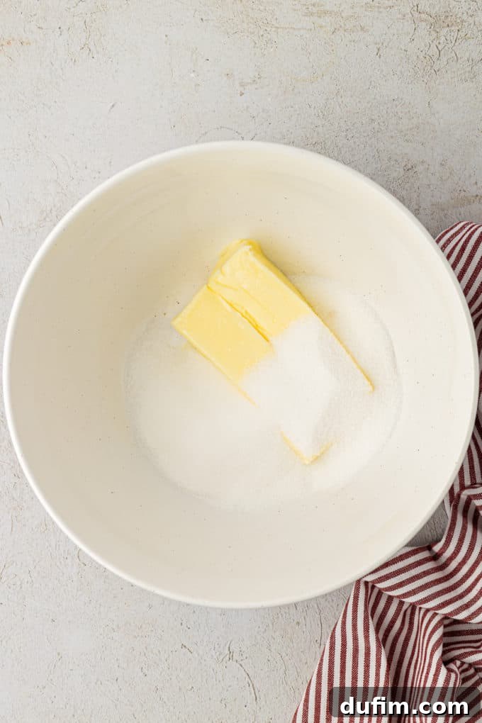THUMBPRINT COOKIES: A TIMELESS DELIGHT 5 Softened butter and granulated sugar sit in a white mixing bowl on a countertop beside a festive red and white striped towel, ready to be creamed together.