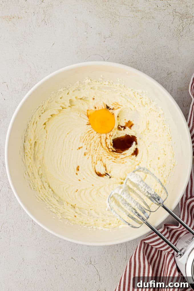 THUMBPRINT COOKIES: A TIMELESS DELIGHT 6 Buttery mixture of butter, sugar, egg yolk, and vanilla extract in a white bowl on a countertop, with an electric mixer resting on the side, showing the ingredients after being thoroughly combined.