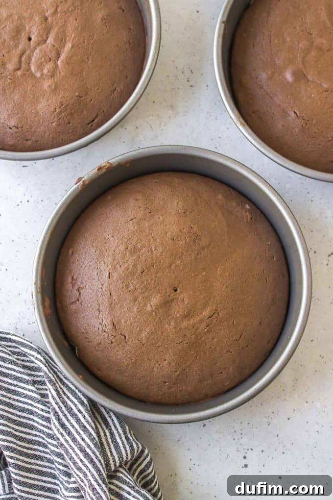 Three cake pans with freshly baked German chocolate cake layers, cooled and ready for assembly, resting beside a black and white striped towel on a countertop.