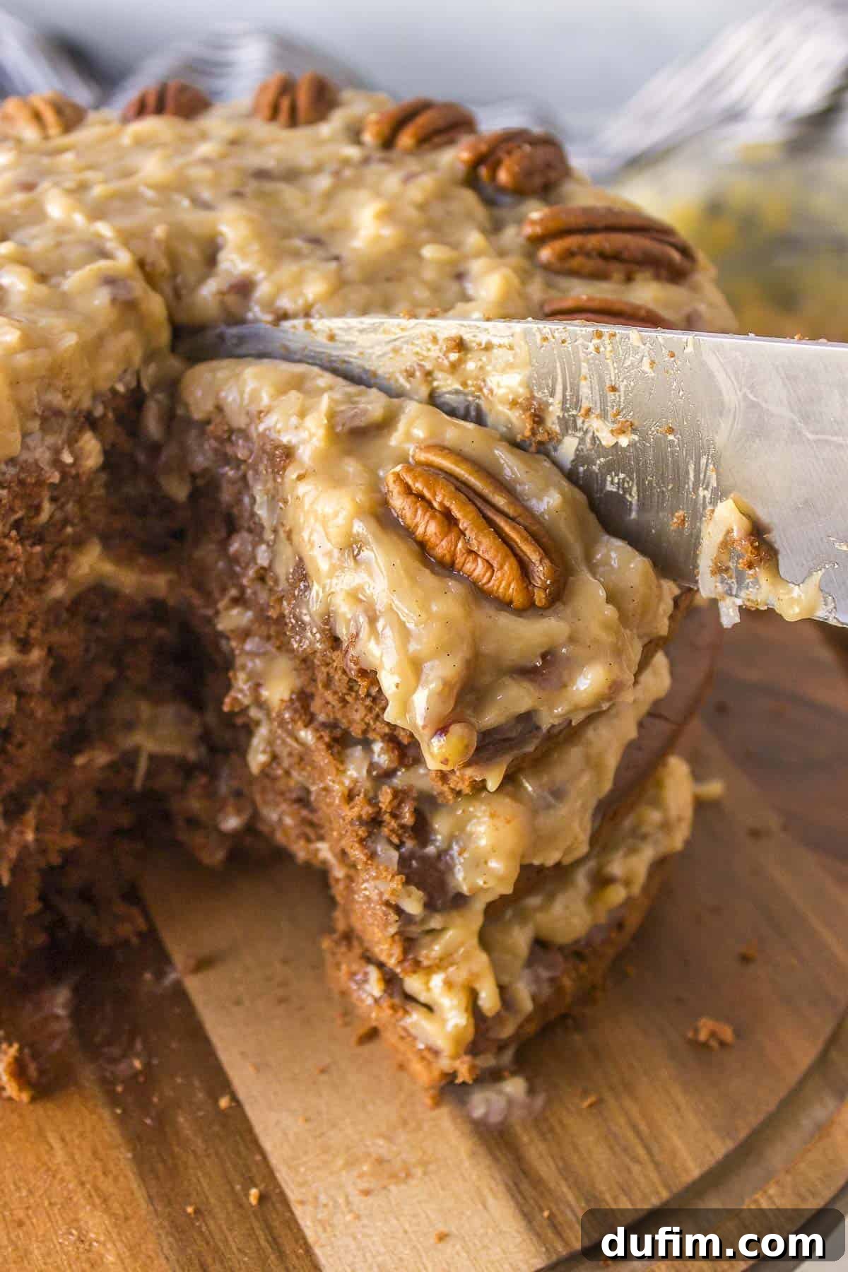 A close-up view of a German chocolate cake on a wooden serving platter, showcasing a slice being carefully cut to reveal its beautiful layers of cake and frosting.