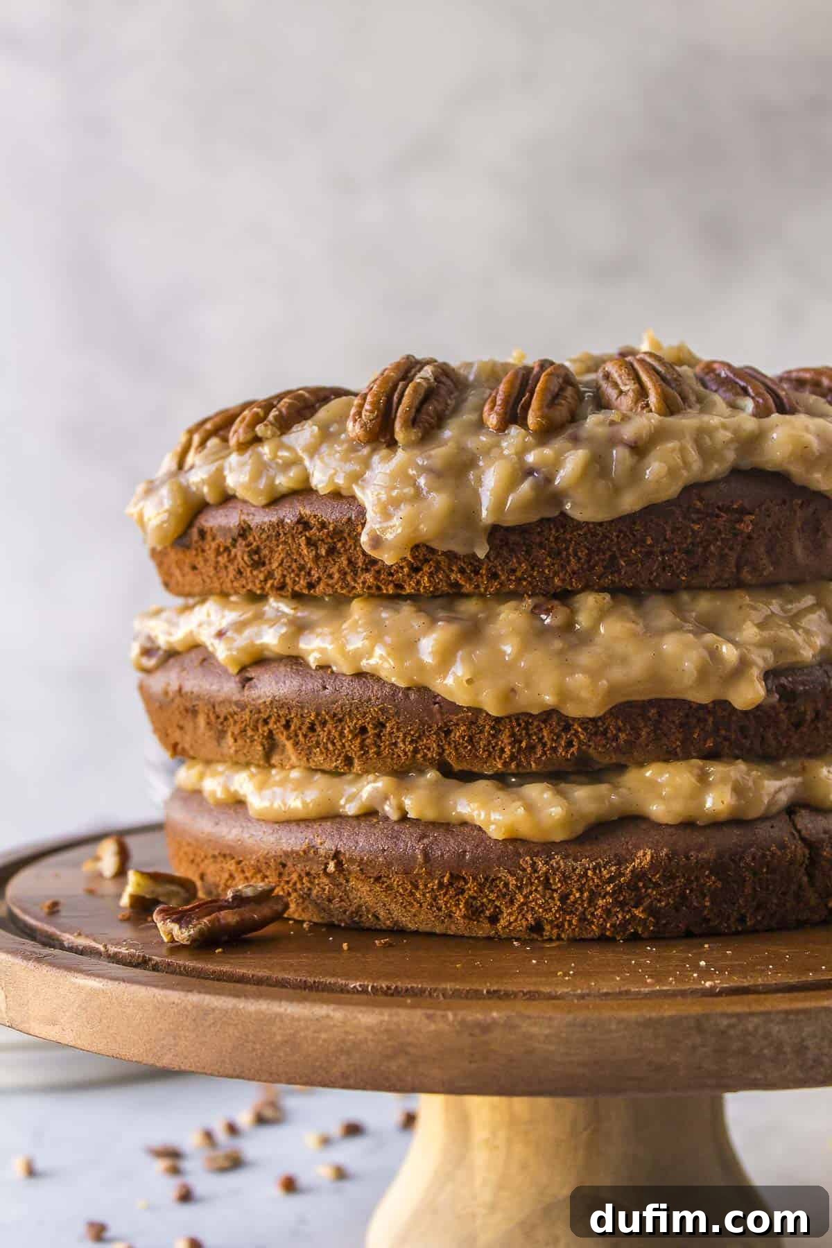 The side view of a German chocolate cake prominently displayed on a wooden serving platter, revealing all its exquisite layers of moist chocolate cake and the rich coconut pecan frosting.