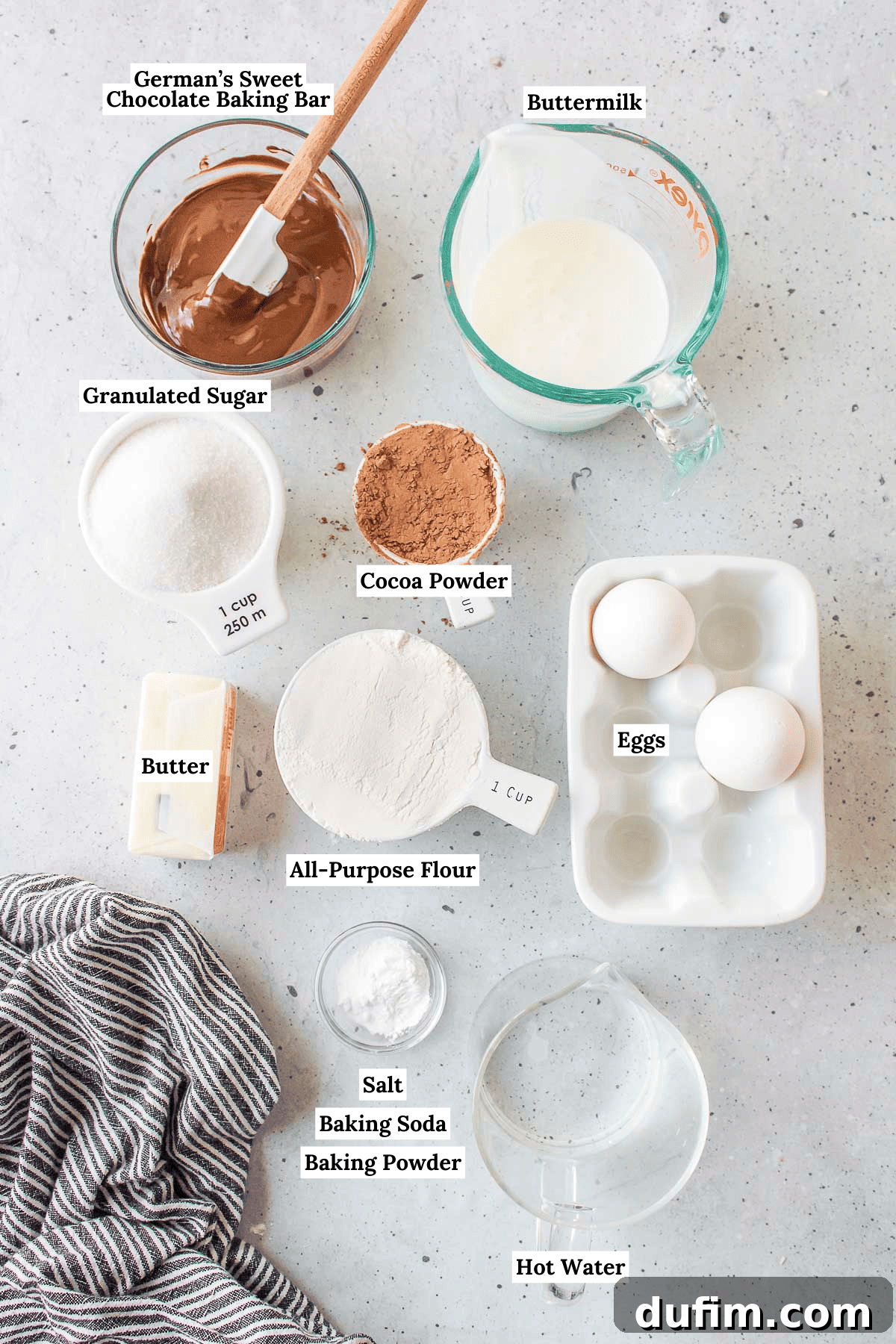 Ingredients for the chocolate cake portion of German chocolate cake, including German's sweet chocolate baking bar, buttermilk, granulated sugar, cocoa powder, butter, all-purpose flour, eggs, salt, baking soda, baking powder, and hot water, neatly arranged on a counter.