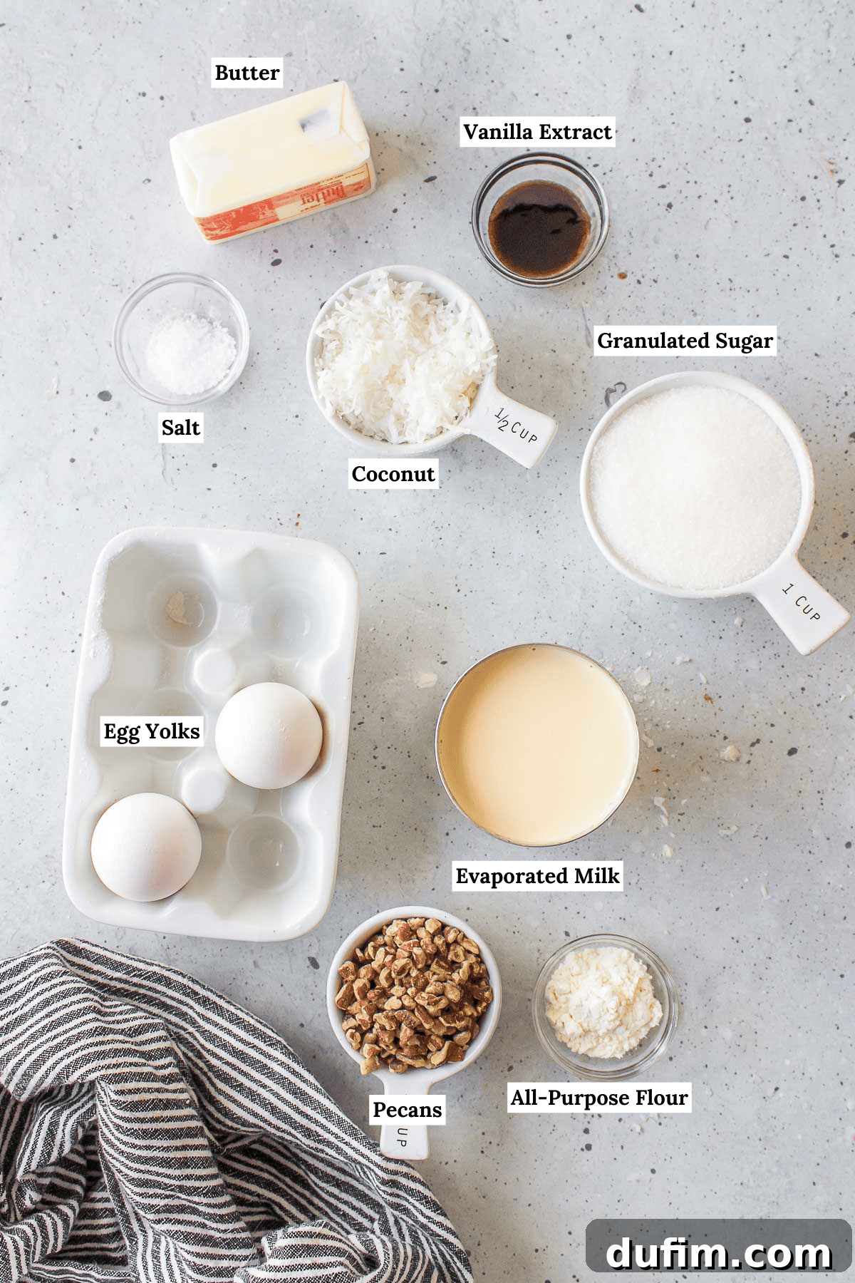 Ingredients for the German chocolate cake frosting, including butter, vanilla extract, salt, shredded coconut, granulated sugar, egg yolks, evaporated milk, pecans, and a small amount of all-purpose flour, neatly displayed.