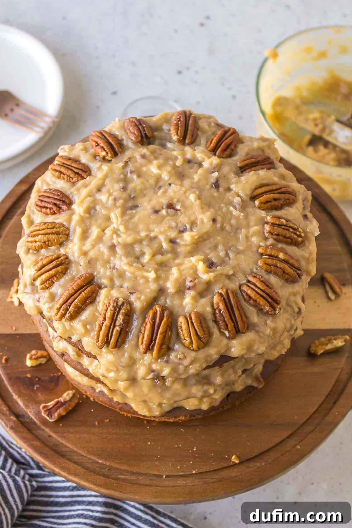 The top view of a beautifully assembled German chocolate cake, generously topped with its signature coconut pecan frosting and elegantly adorned with a ring of whole pecans on a rustic wooden cake platter.