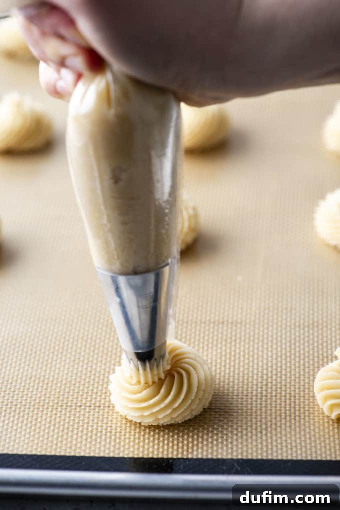 A baking sheet lined with a silicone mat, expertly covered with numerous fully formed butter cookie swirls, showcasing consistent piping technique.