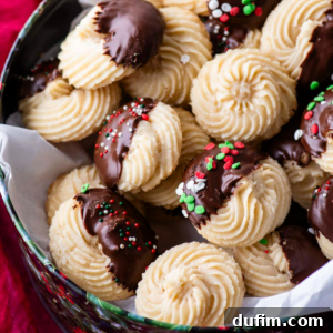 A festive Christmas tin full of butter cookies, some plain and some dipped half in chocolate, with a few adorned with red, green and white sprinkles.