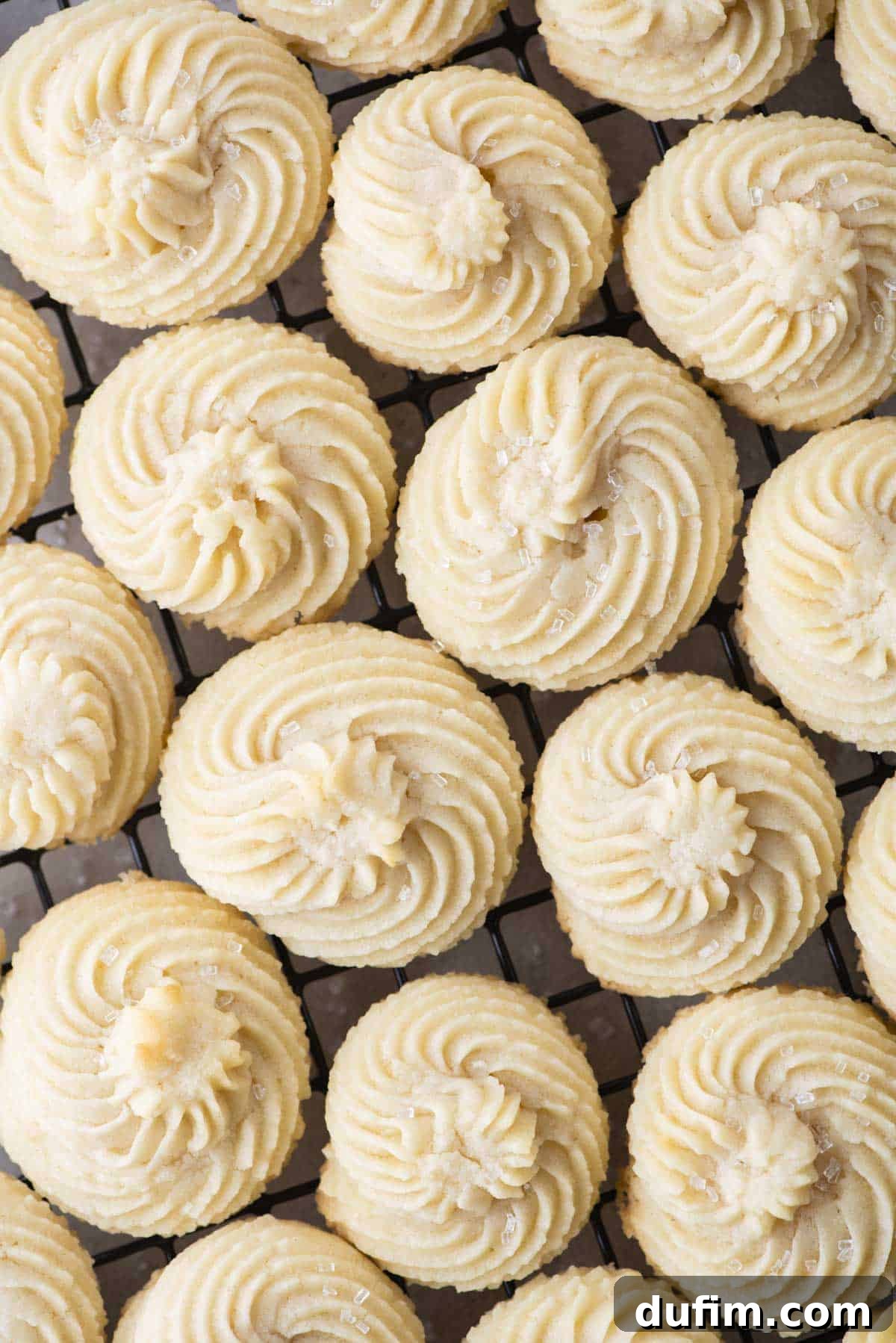 Close-up view of perfectly piped, plain butter cookies arranged in neat rows on a baking sheet, showcasing their intricate and consistent designs.