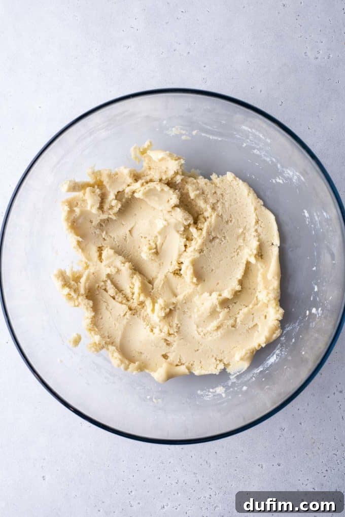 Smooth butter cookie dough fully mixed together and cohesive in a glass bowl, ready for the next step of piping.