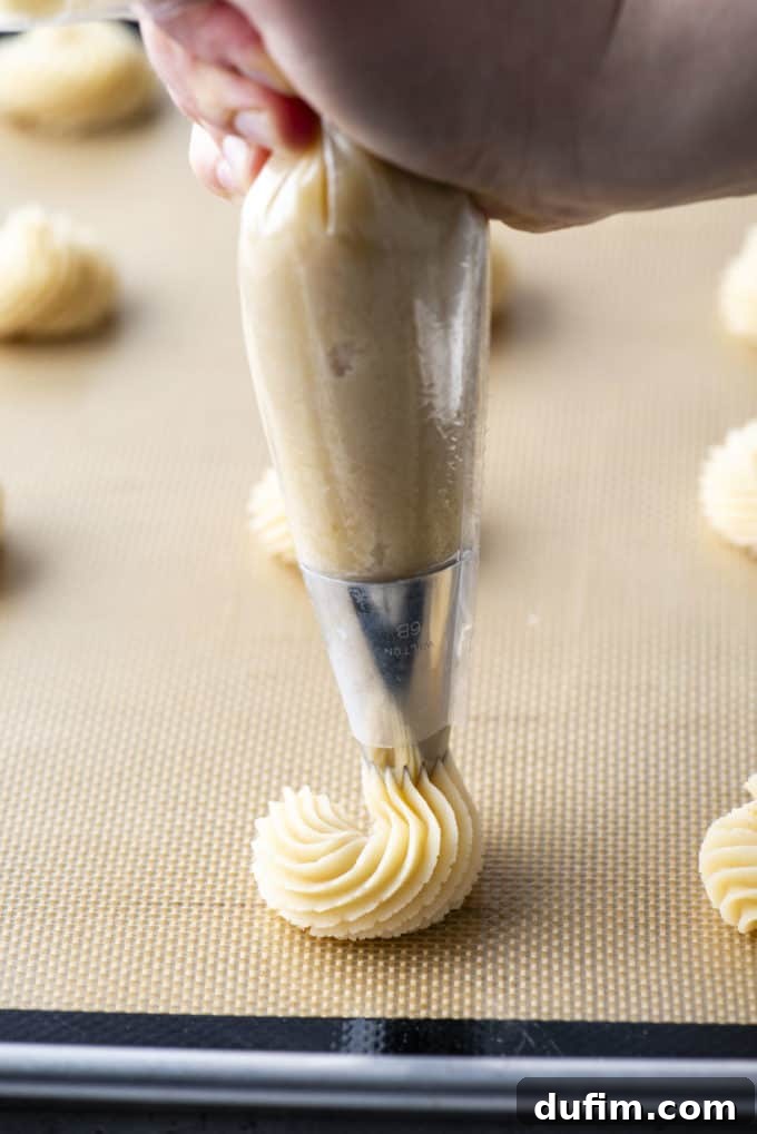 Butter cookies being expertly piped onto a cookie sheet lined with a silicone mat, showing the initial stages of forming a swirl pattern.